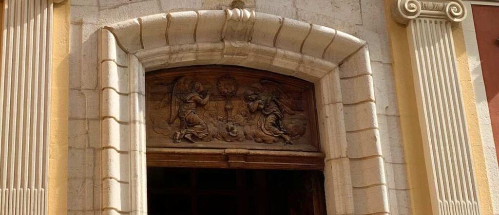 The wooden panel (cartouche) above the doors depicts the worship of the sacrament by two angels